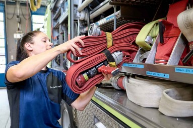 Berufsfeuerwehrfrau Eine Berufsfeuerwehrfrau hebt ein Schlauchpaket aus dem Tanklöschfahrzeug