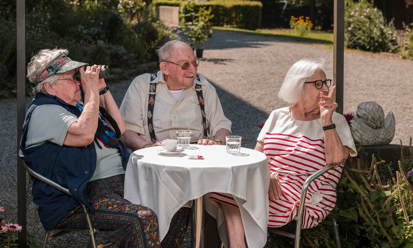 Bewohner*innen des Gesundheitszentrums für das Alter Klus Park sitzen an einem Tisch in der Parkanlage und geniessen die Gemeinschaft.