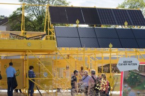 Besucherinnen und Besucher im gelben Ausstellungspavillon mit Solarpanels auf Dach