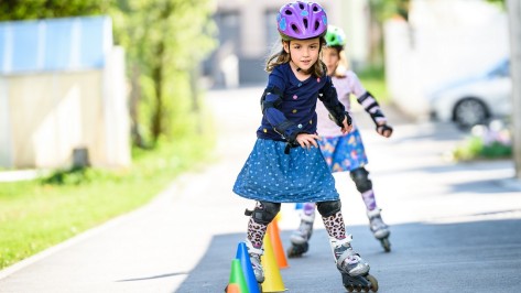 Zwei Mädchen fahren mit Rollschuhen um Hüttchen.