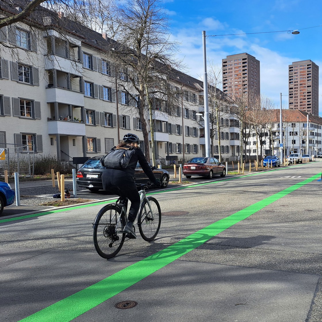 Eine Velofahrende auf einer Strasse, welche links und rechts ein grünes Band markiert hat. 