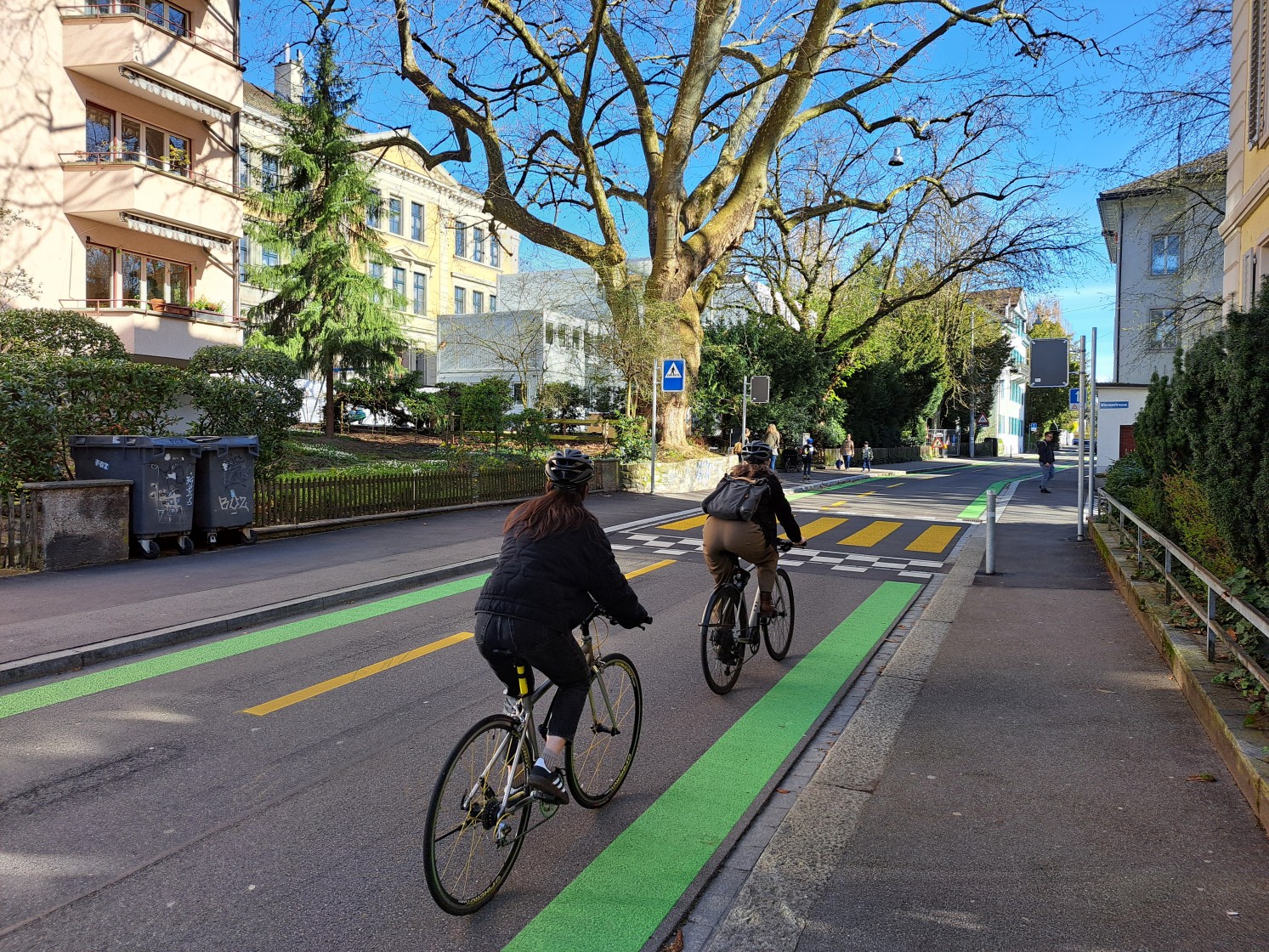 Zwei Velofahrende auf einer Strasse, welche links und rechts ein grünes Band markiert hat. 