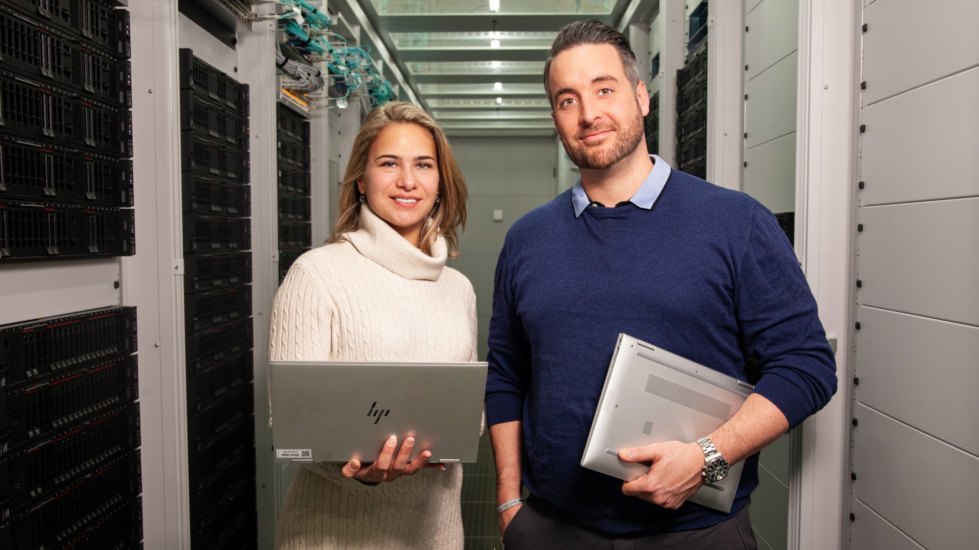 Ein Mann und eine Frau mit einem Laptop in der Hand stehend im Serverraum.